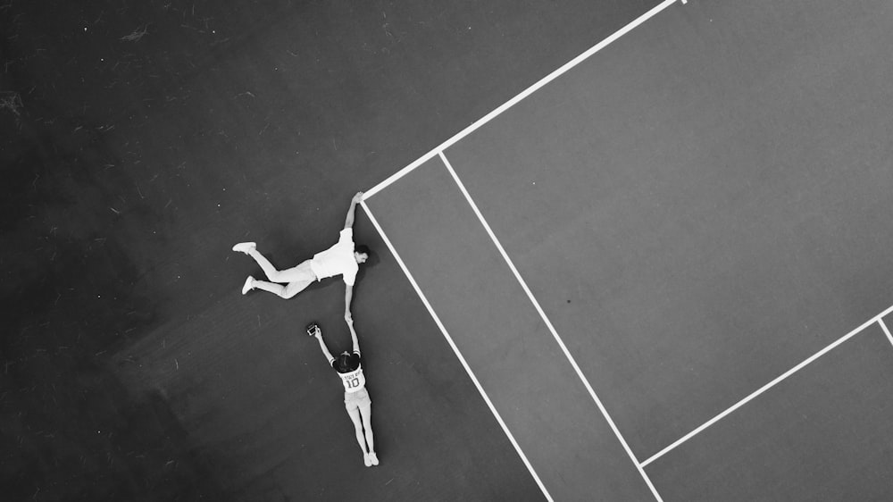 Graustufenfotografie einer Frau, die auf dem Tennisplatz die Hand einer Frau hält