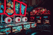Brightly lit arcade machines with superhero-themed graphics featuring popular characters. The machines are adorned with colorful lights and feature comic book imagery, creating a vibrant and playful atmosphere.