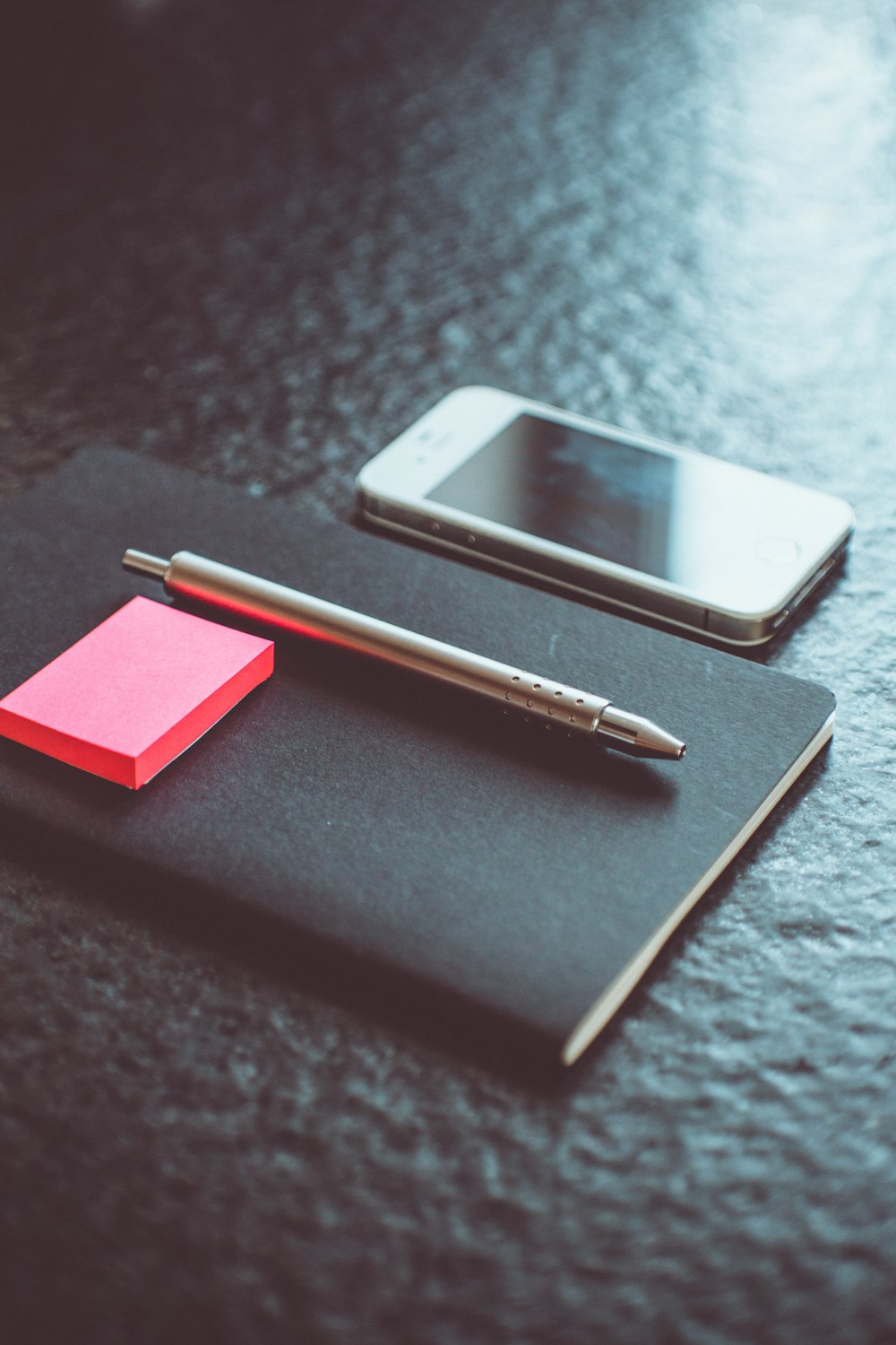 grey click pen on black planner beside white iPhone