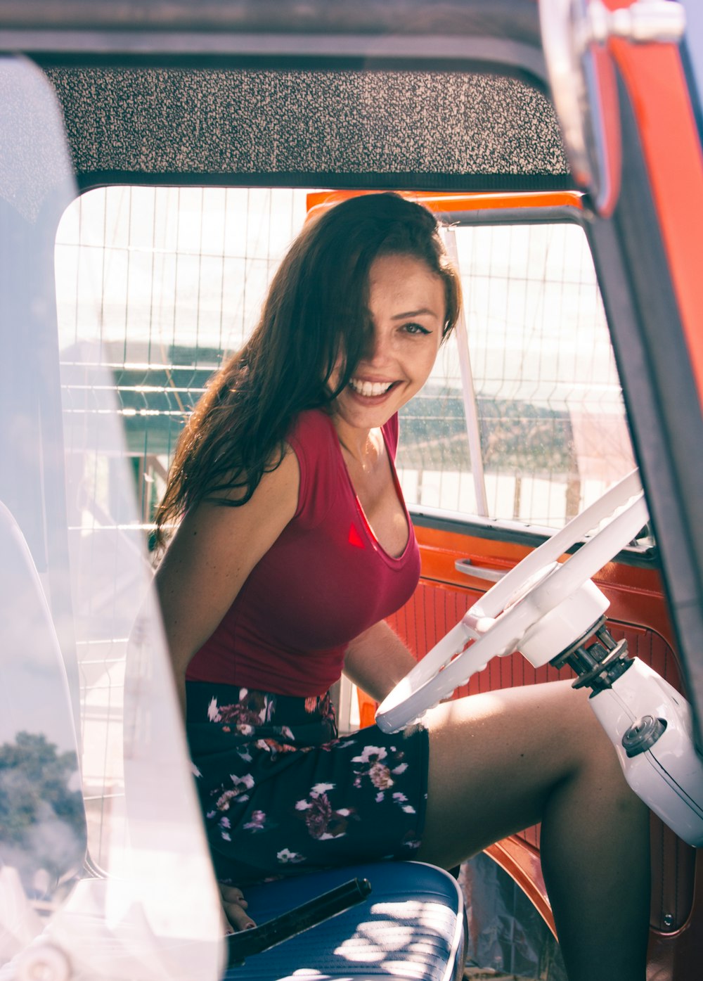 Mujer con camiseta sin mangas roja y falda floral multicolor mientras está sentada dentro del vehículo