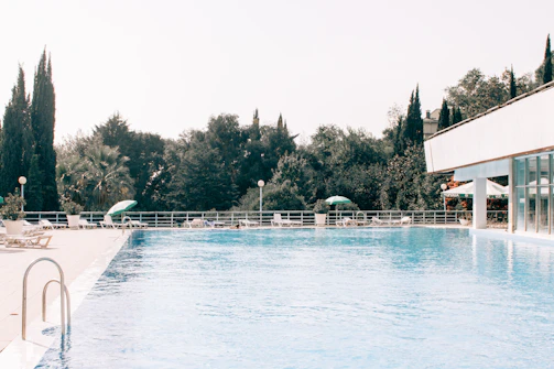Swimming pool area surrounded by greenery and comfortable lounge chairs.