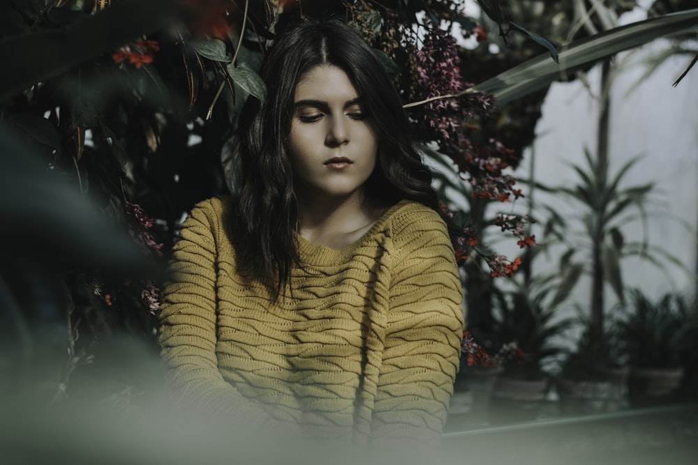 woman in yellow turtleneck sweater standing beside red flowers