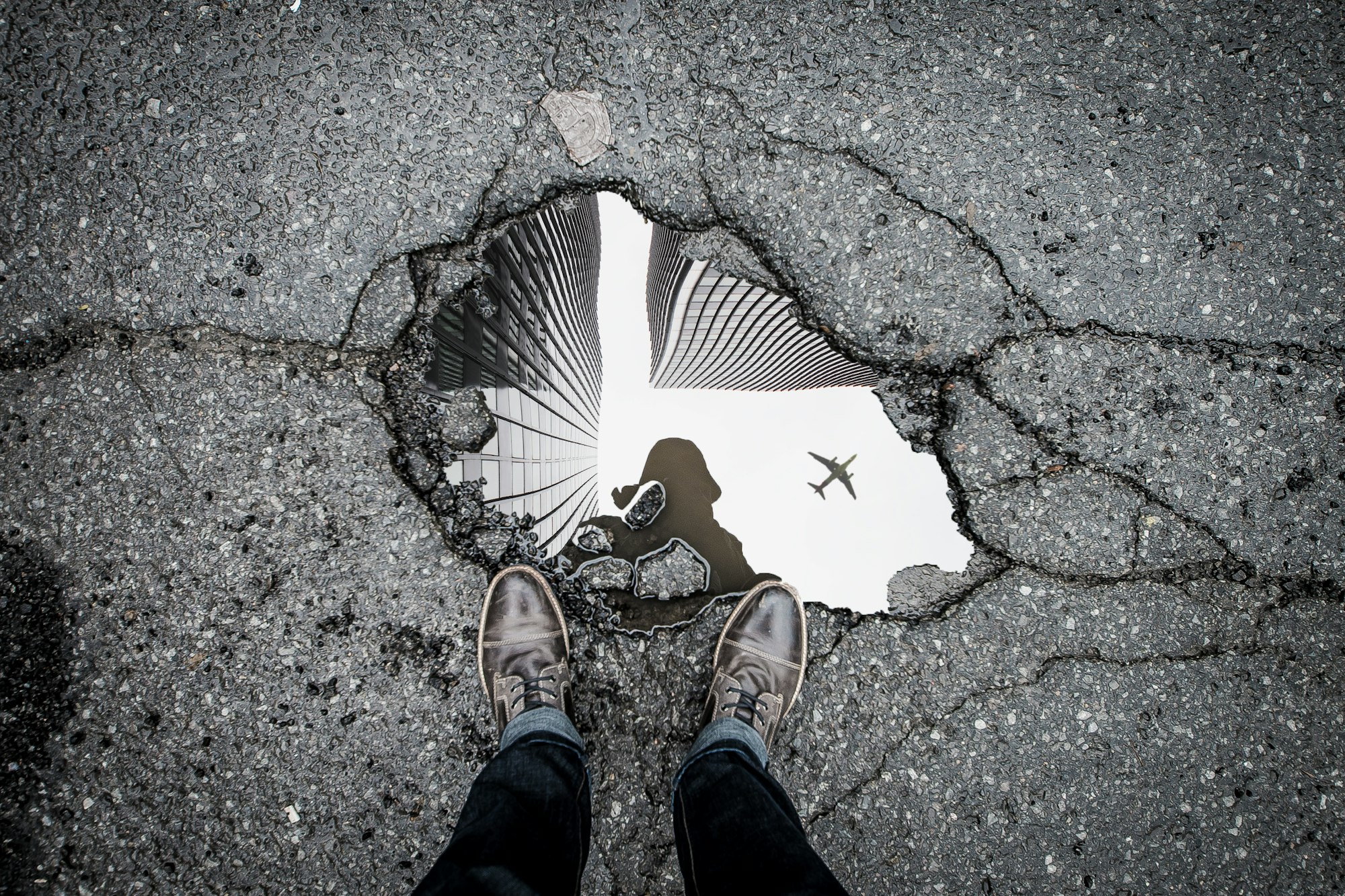 A shot of a puddle, which is reflecting tall buildings and an airplane.