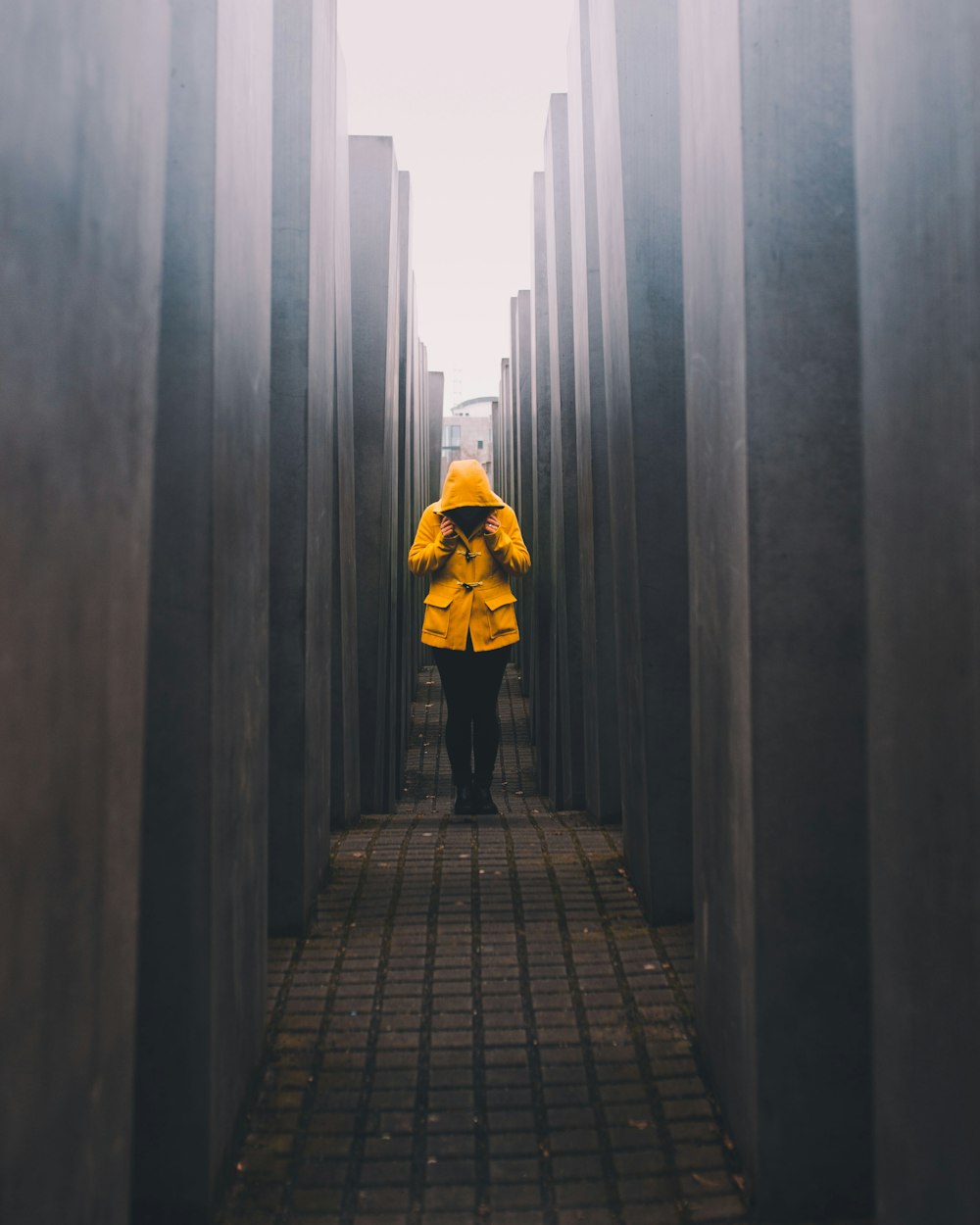 person in mustard hoodie and black pants standing on pathway