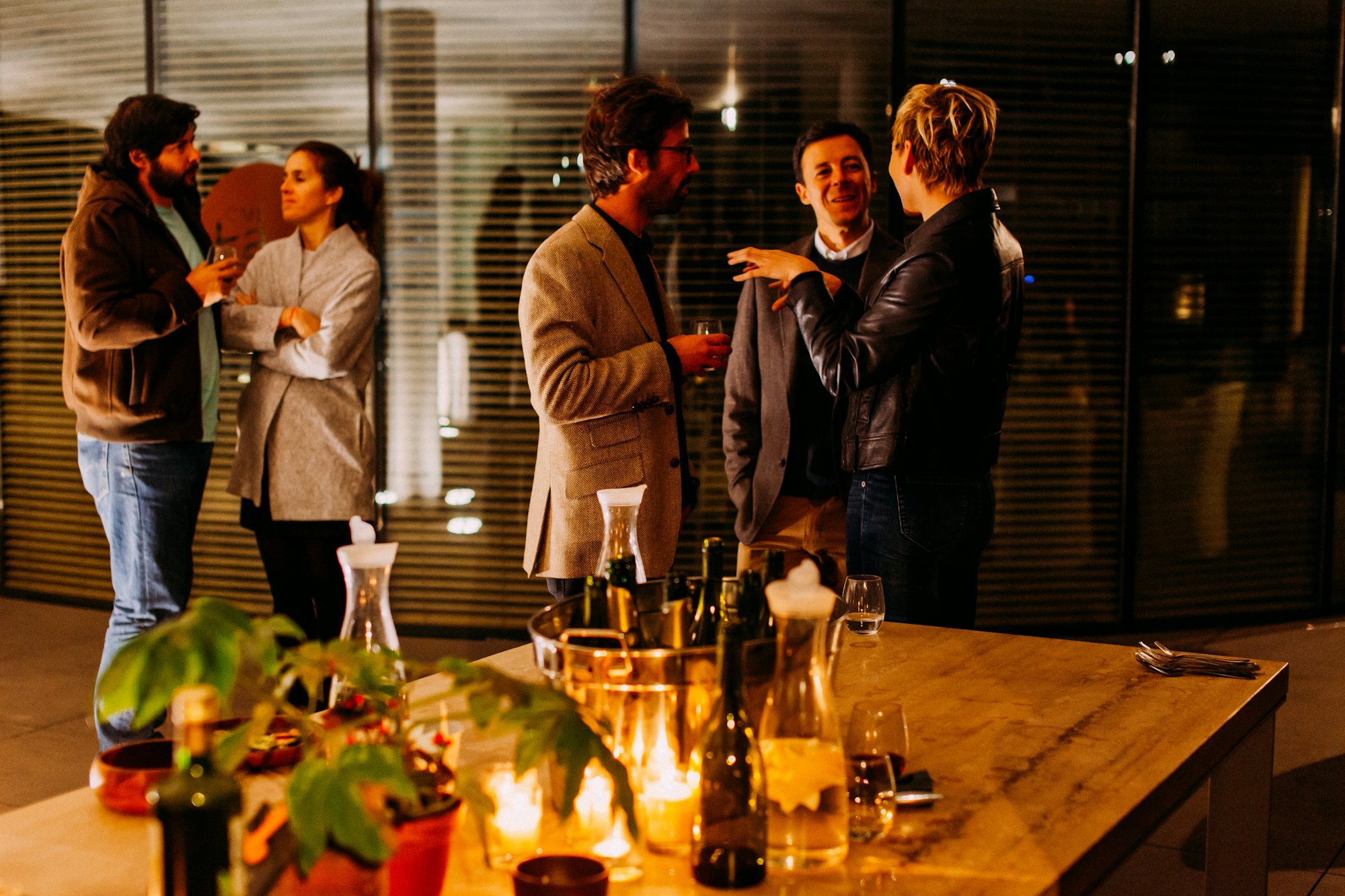 Five people stand near a table with drinks in their hands as they chat.