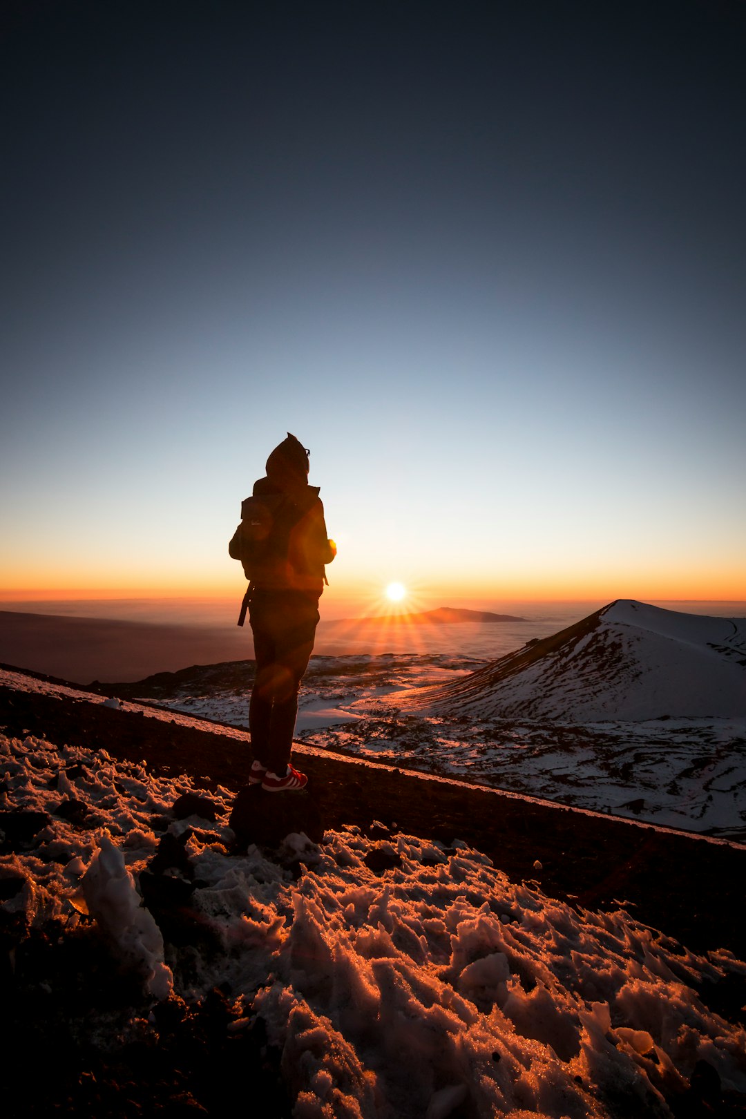 person carrying bag standing on snow coated ground looking at sun