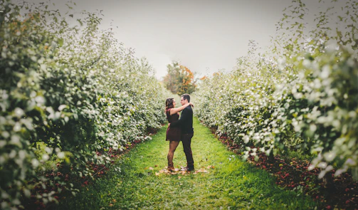 A romantic outdoor engagement photo session with a couple holding hands near a blooming orchard.