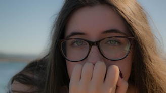A close-up of a person wearing sleek, modern eyeglasses with a soft pastel background.