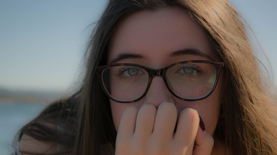 A close-up of a person wearing sleek, modern eyeglasses with a soft pastel background.