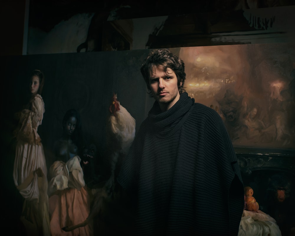 man in black poncho standing in front of paintings