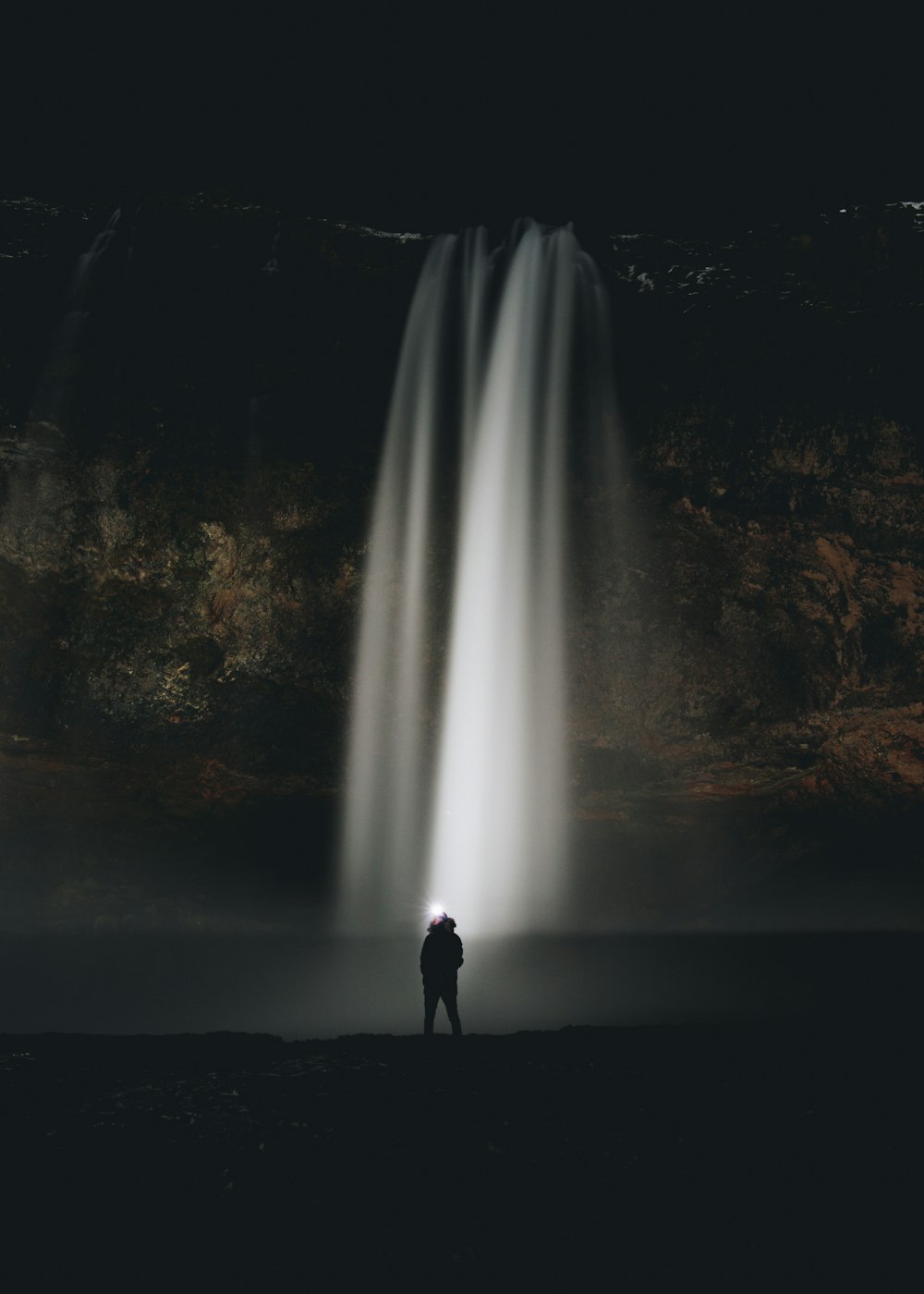 homme debout devant des chutes d’eau pendant la nuit