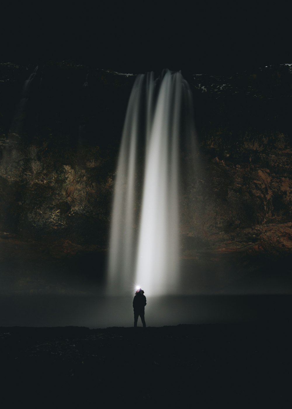 夜の滝の前に立つ男