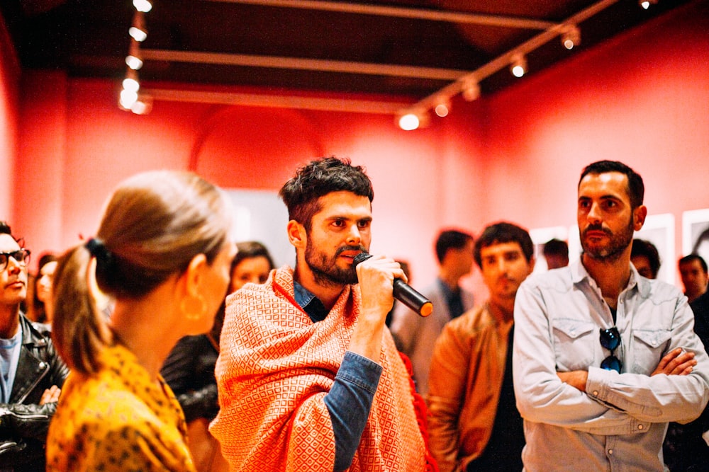 man using microphone speaking surrounded of people inside the room