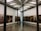 An art gallery with framed photographs hung on the walls in a bright room. The pictures display various human figures and scenes. The gallery features exposed beams on the ceiling and tall, dark columns within the space. Two people are present, observing the art.