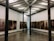 An art gallery with framed photographs hung on the walls in a bright room. The pictures display various human figures and scenes. The gallery features exposed beams on the ceiling and tall, dark columns within the space. Two people are present, observing the art.