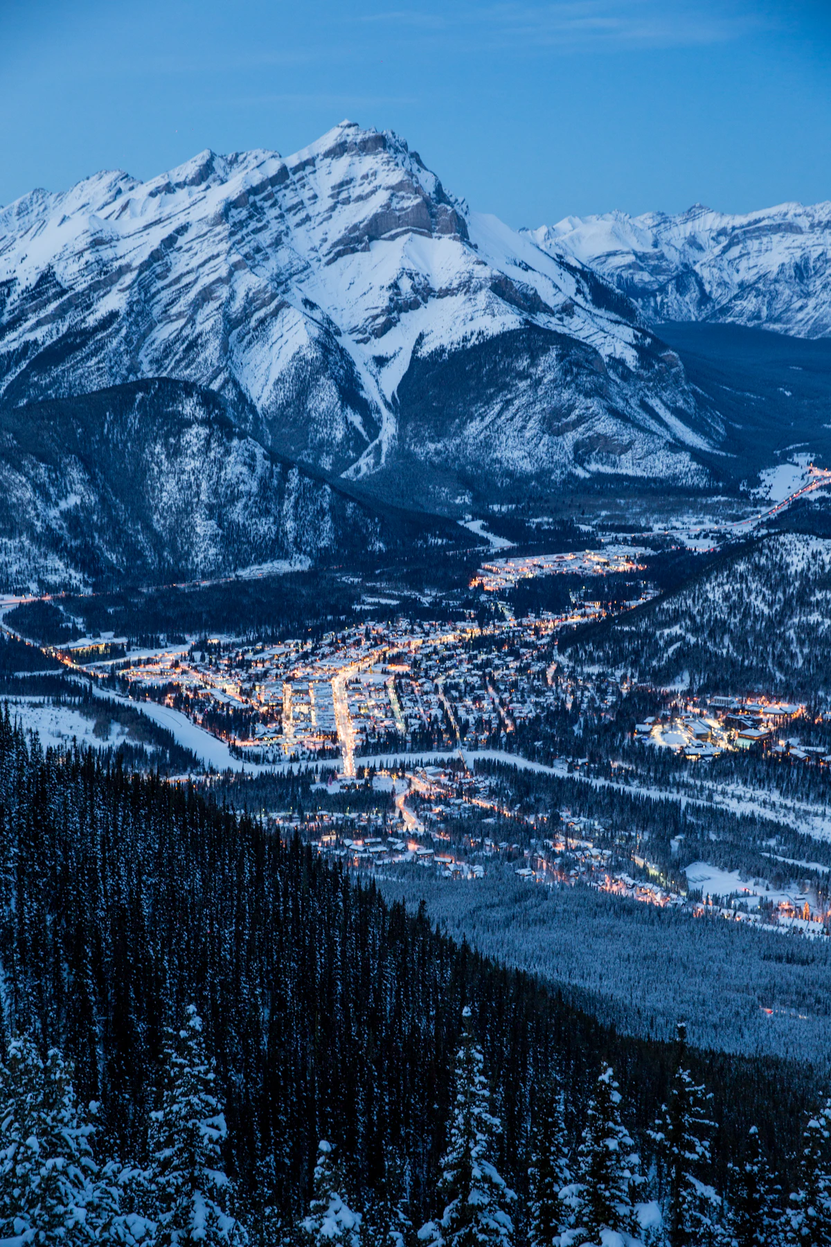 Village lights below a snow-capped mountain at dusk