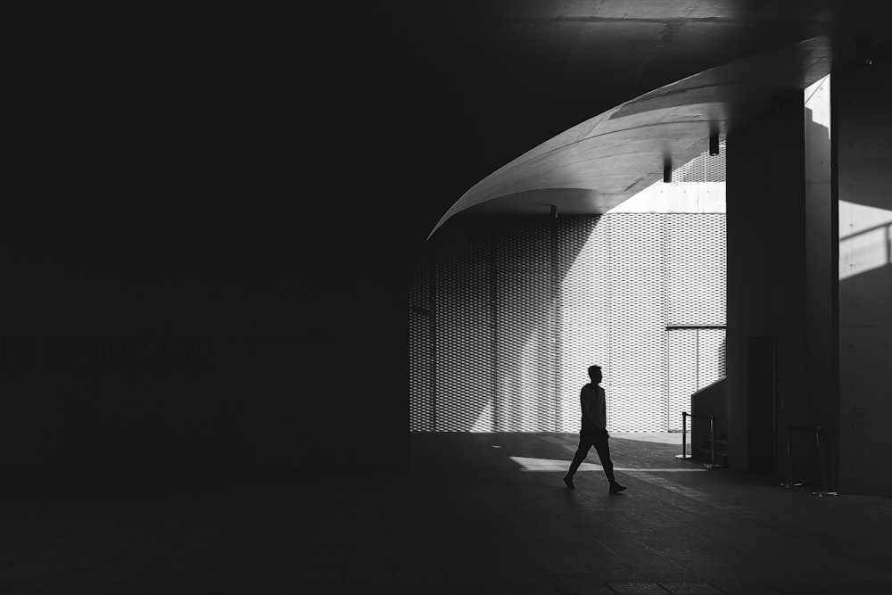 silhouette photography of man walking on floor beside post
