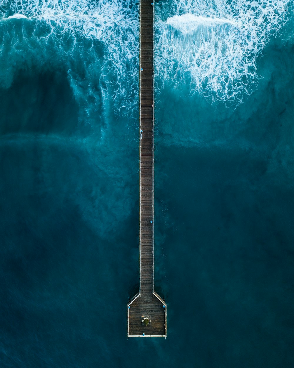 Fotografía aérea de la persona de pie en el muelle junto al mar durante el día