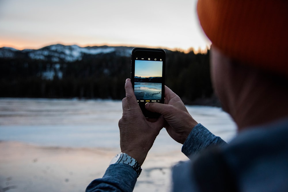 person holding smartphone taking picture of body of water