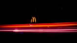 Bright, colorful light trails streak horizontally across a dark background, with a recognizable fast food logo illuminated above them.