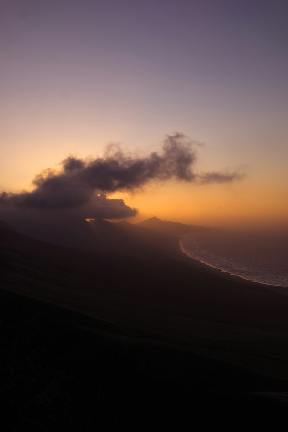 Berg in der Nähe des Meeres unter weißen Wolken während der goldenen Stunde