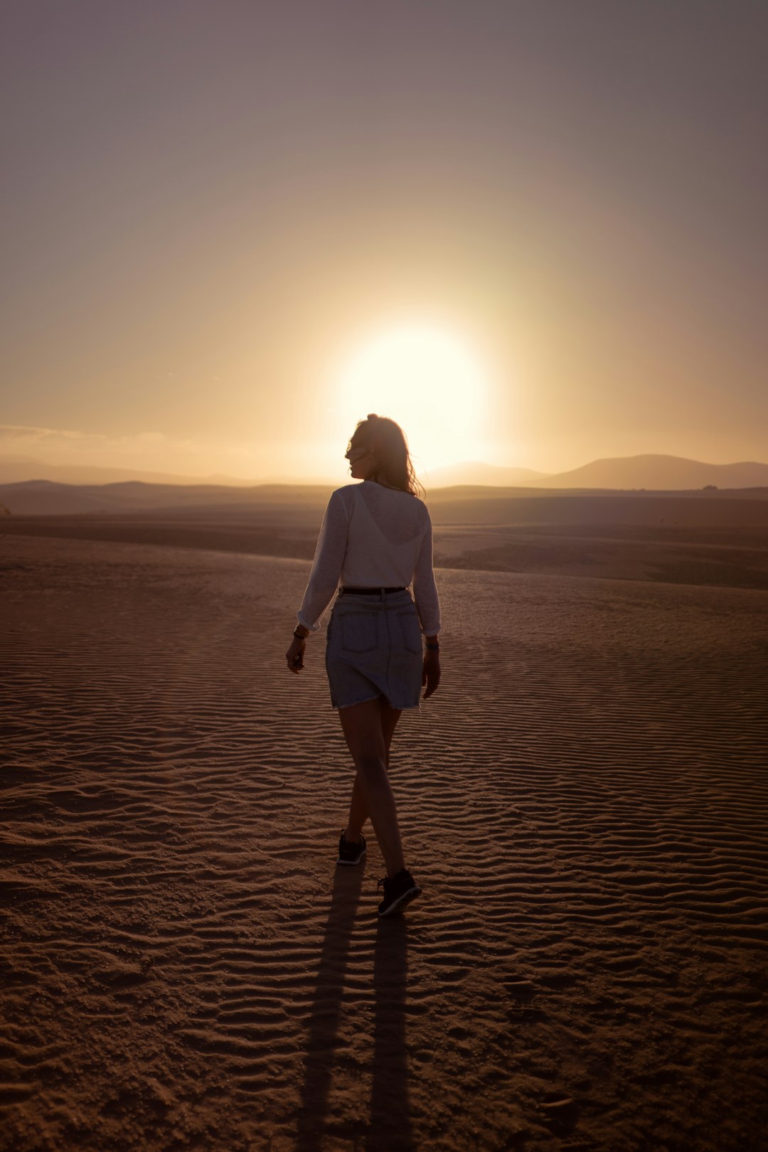 woman in white shirt and blue skirt walking on desert