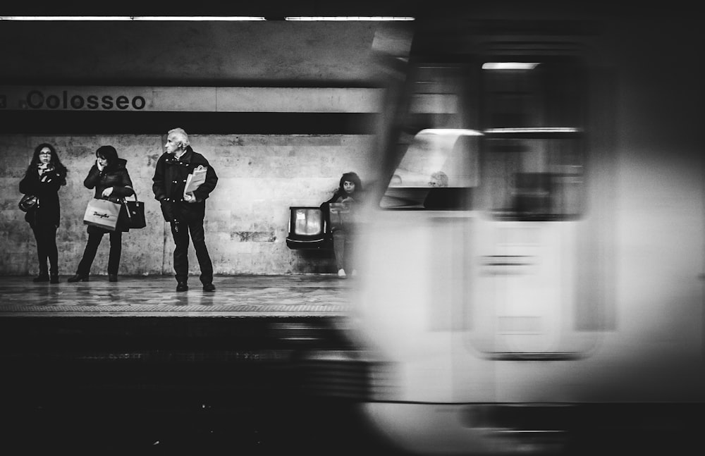 grayscale photo of three people standing on train station