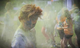 A family holding hands while walking through a vibrant cloud of blue and pink powder, all smiling happily.