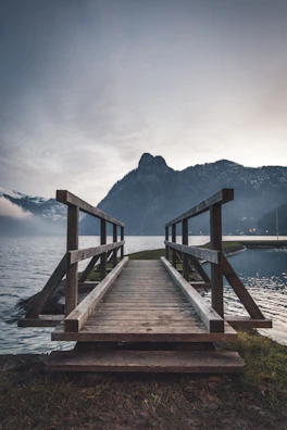 Hikers crossing a wooden bridge over a rushing mountain stream at sunrise.