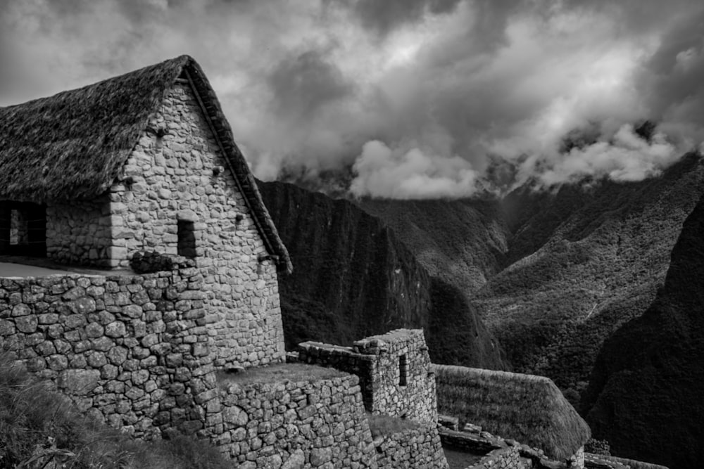 grayscale photography of house near mountain under the cloudy sky