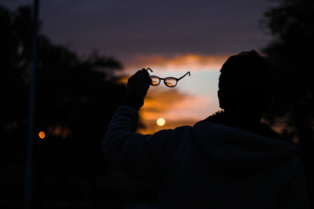 silhouette photo of man holding eyeglasses