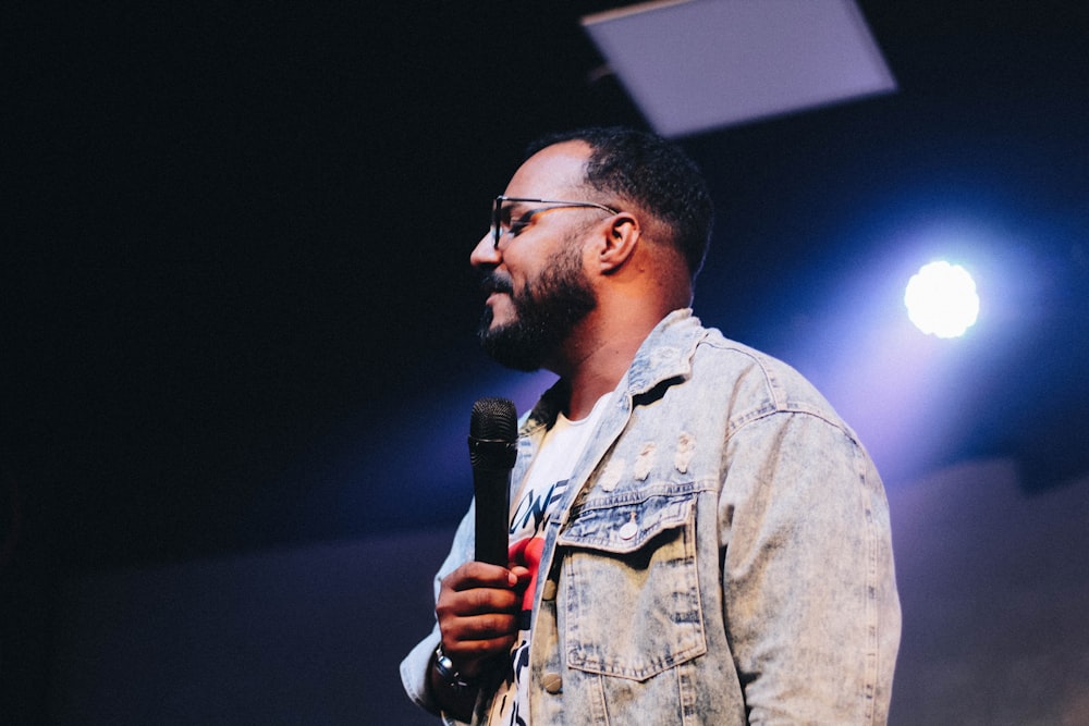 Homme debout portant une veste boutonnée en jean bleu tout en tenant un microphone