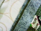 A collection of colorful fabric patterns featuring geometric shapes and floral designs. The fabrics include a range of colors such as white, beige, blue, green, and black with intricate and varying patterns.