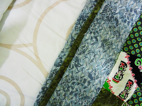 A collection of colorful fabric patterns featuring geometric shapes and floral designs. The fabrics include a range of colors such as white, beige, blue, green, and black with intricate and varying patterns.