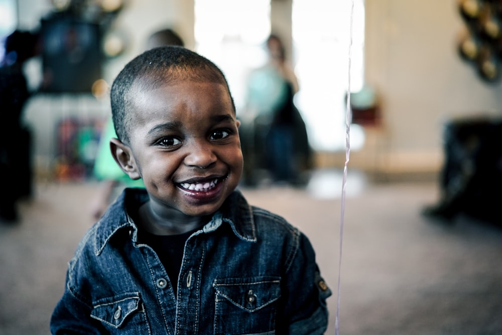 grayscale photo of boy wearing denim jacket smiling near white string