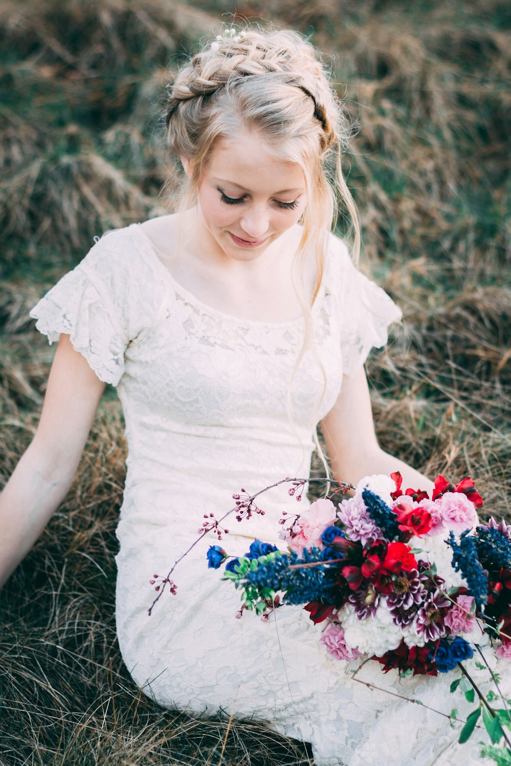 woman wearing white lace dress with flower bouquet sitting on grass at daytime