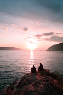 two persons sitting on rock during dawn