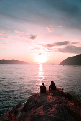 two persons sitting on rock during dawn