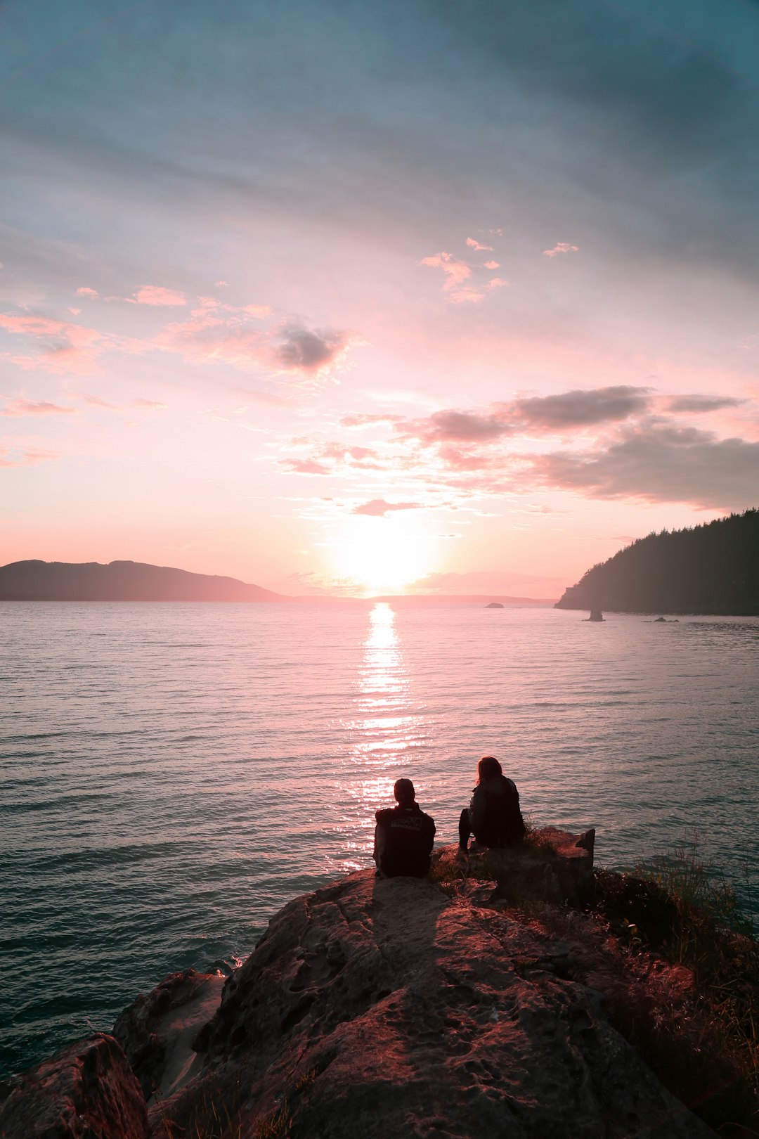 two persons sitting on rock during dawn