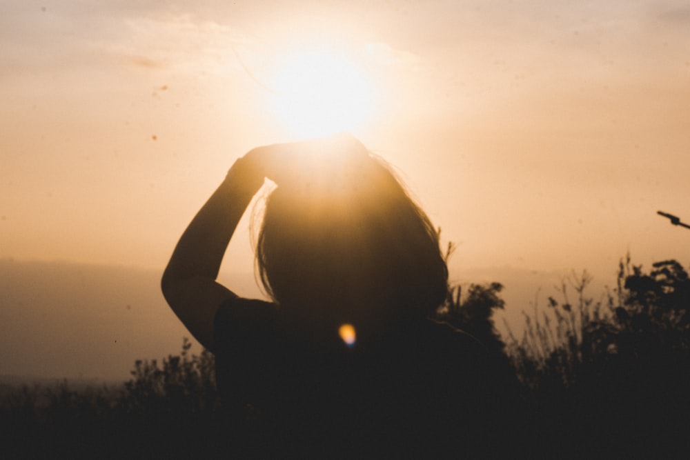 silhouette photo of person standing near plants during golden hour