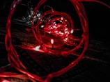 A close-up view of red LED lights intertwined with wires, creating a spiral effect against a dark background. The lights emit a warm, glowing illumination, forming intricate patterns and reflections.