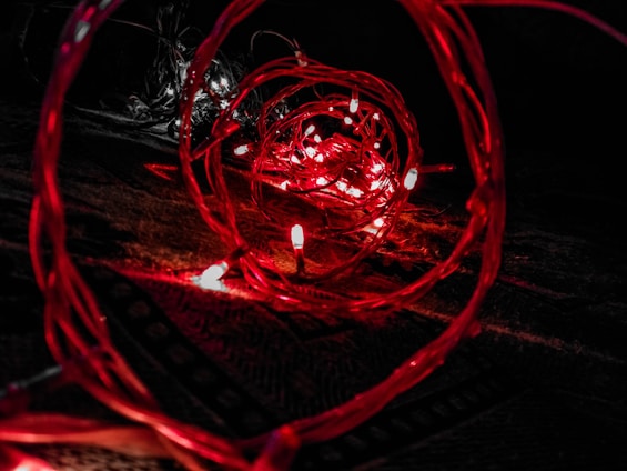 A close-up view of red LED lights intertwined with wires, creating a spiral effect against a dark background. The lights emit a warm, glowing illumination, forming intricate patterns and reflections.