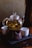 A glass teapot filled with tea leaves is placed on a ceramic warmer, accompanied by two white tea cups on a textured black tray. The setting is dimly lit, creating a cozy ambiance.