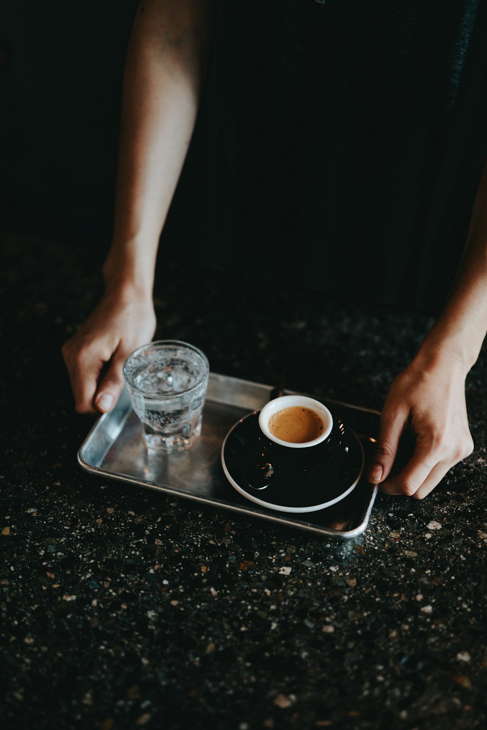 person holding tray with drinking glass and coffee cup