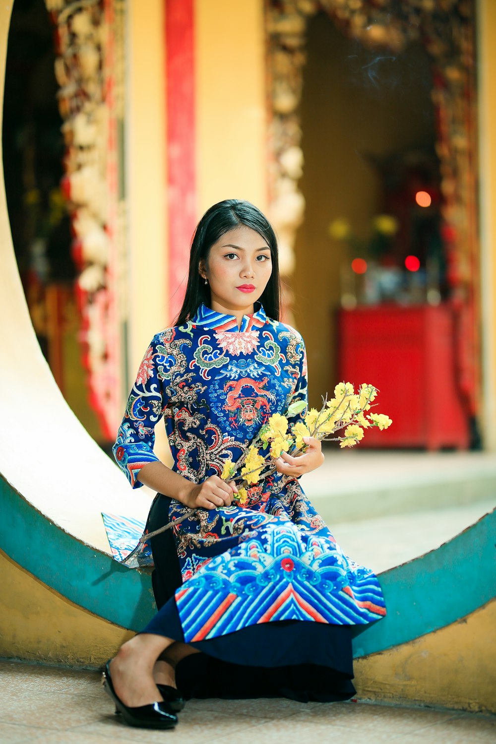 woman sitting on green concrete surface holding flower