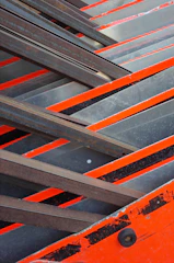 Close-up of matte charcoal steel beams intersecting with bright orange construction accents.