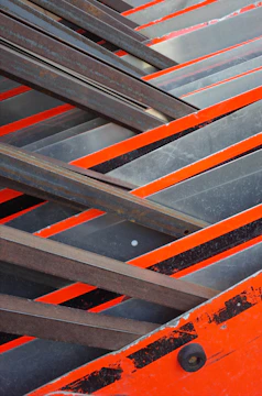 Close-up of matte charcoal steel beams intersecting with bright orange construction accents.