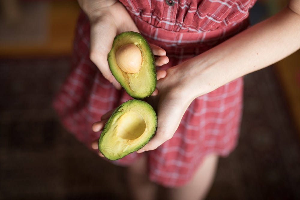 person holding two sliced avocados