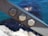 Three metal hexagonal bolts are fastened on a steel beam with an out-of-focus background of blue water and rocks.