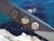 Three metal hexagonal bolts are fastened on a steel beam with an out-of-focus background of blue water and rocks.